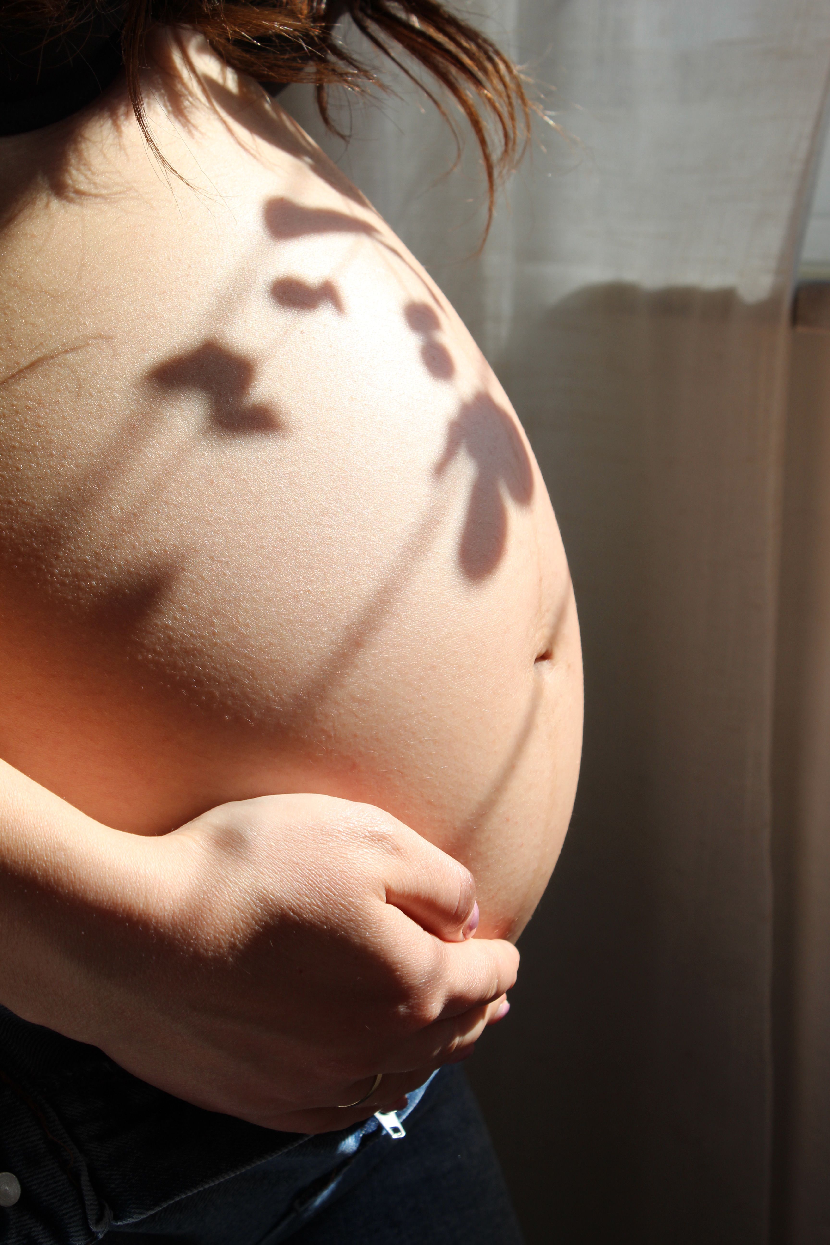 Pregnant woman in soft sunlight, holding her belly